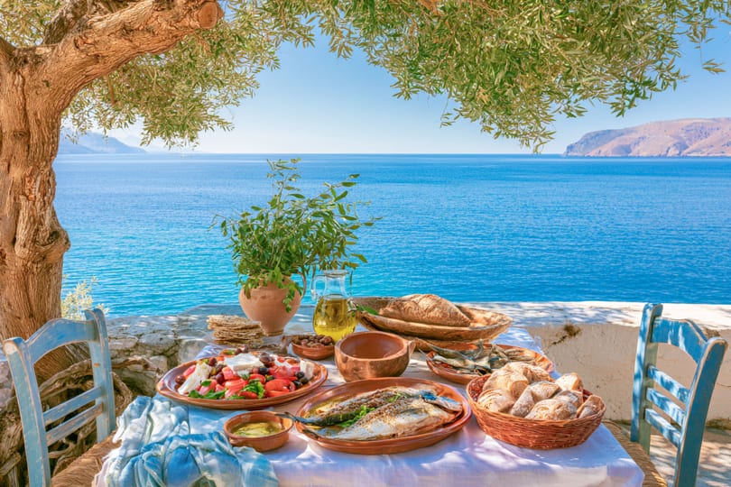 A Mediterranean meal with fresh fish, salad, and bread on a table overlooking the blue sea.