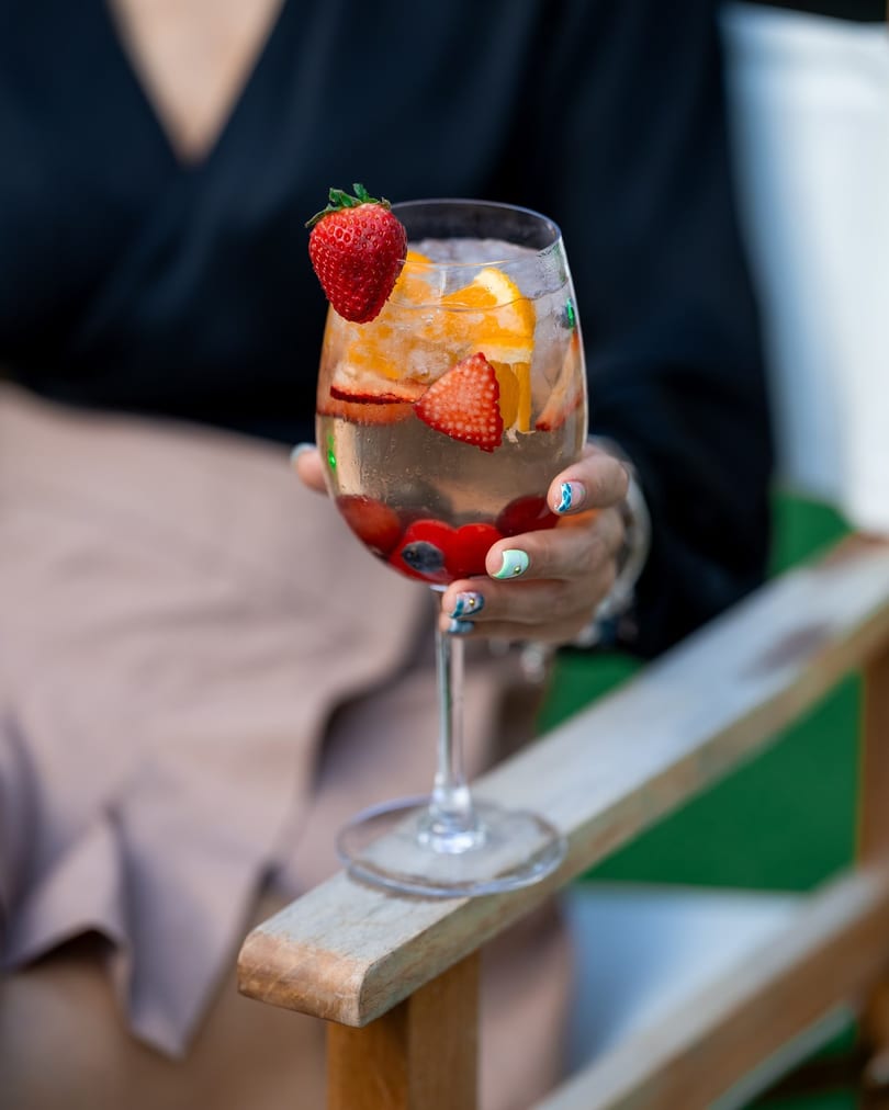 A person holds a wine glass filled with a refreshing drink, strawberries, and orange slices.