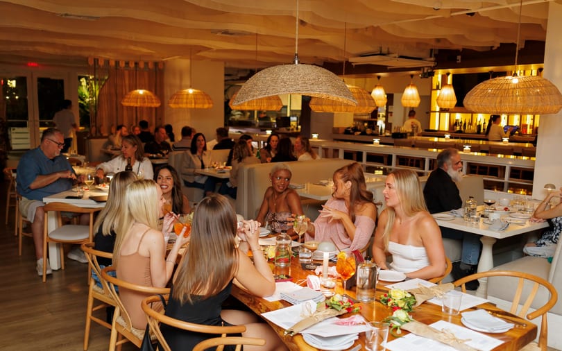 Diners enjoying a meal in a warmly lit restaurant with woven pendant lights and a bar.